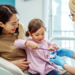 child at dentist for her first dental visit sitting on mother's lap in dental chair