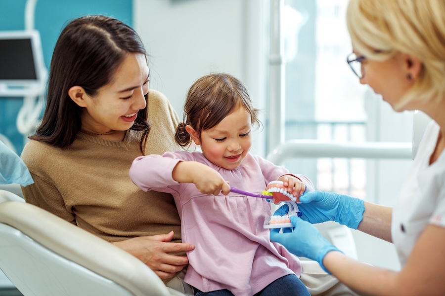 child at dentist for her first dental visit sitting on mother's lap in dental chair